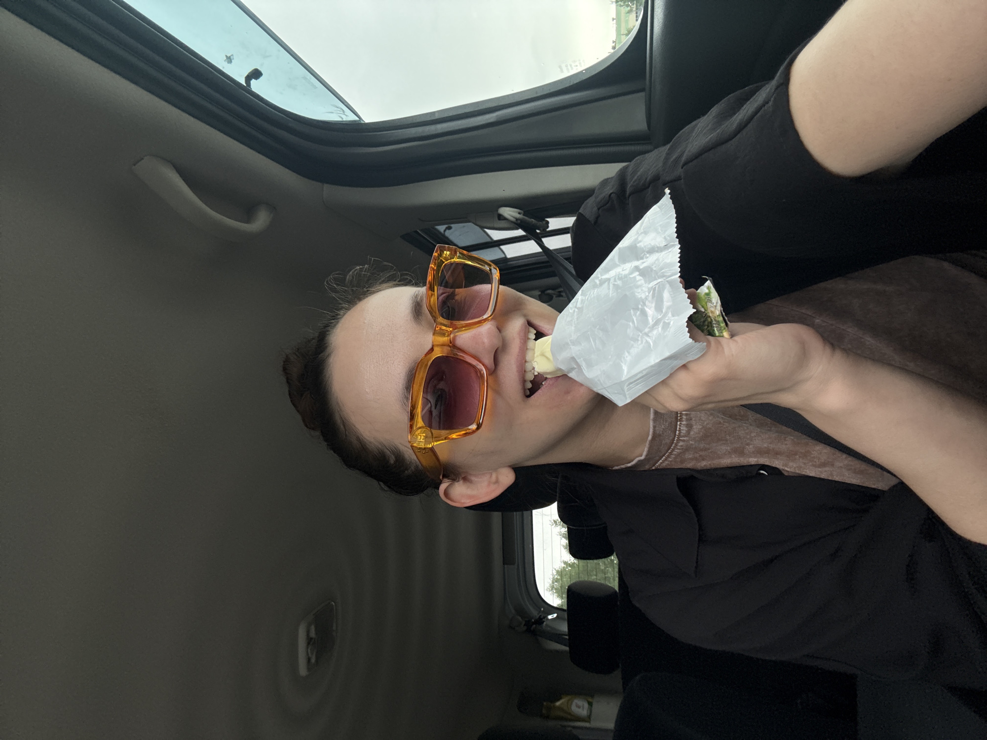Person in orange sunglasses eats from bag in car
