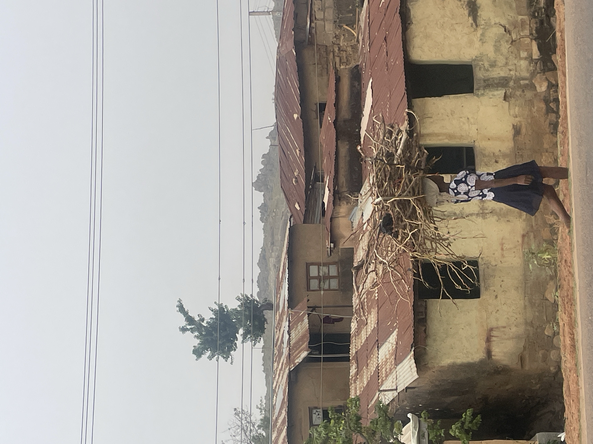 Woman carries branches near weathered building in Jos, Nigeria