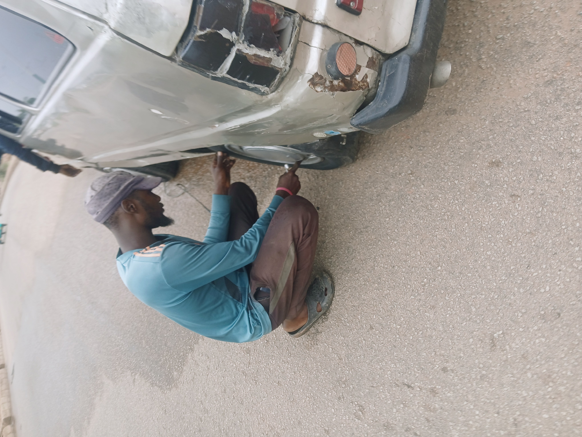 Man performs vehicle maintenance on gray car in Bukuru