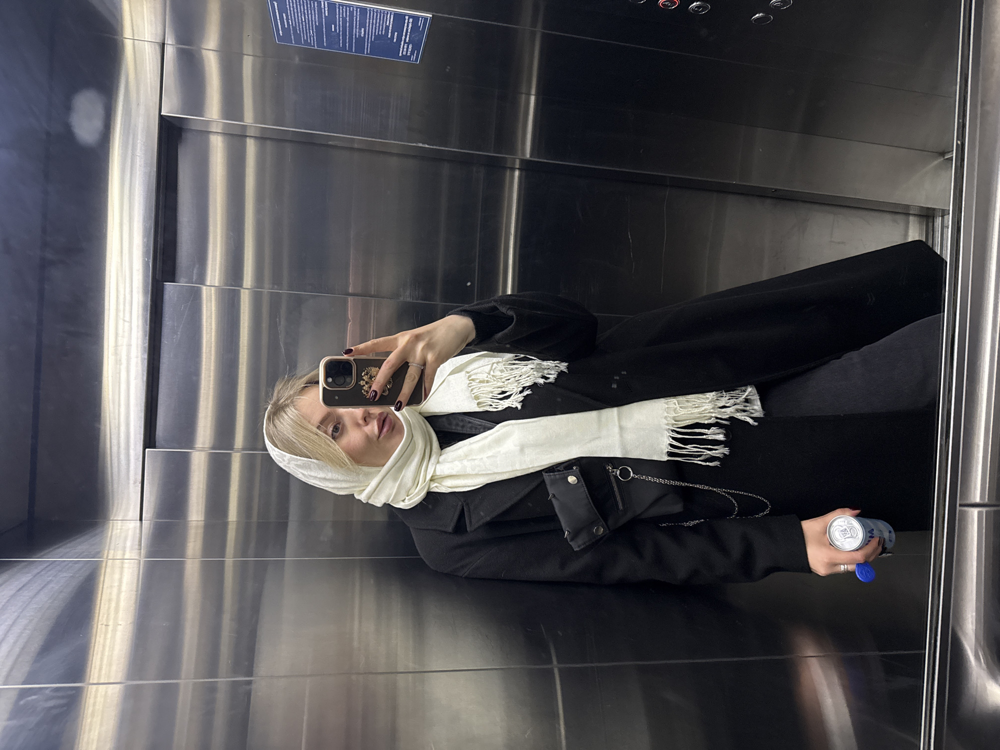 Woman with beverage observed in mirrored elevator in Krasnoyarsk