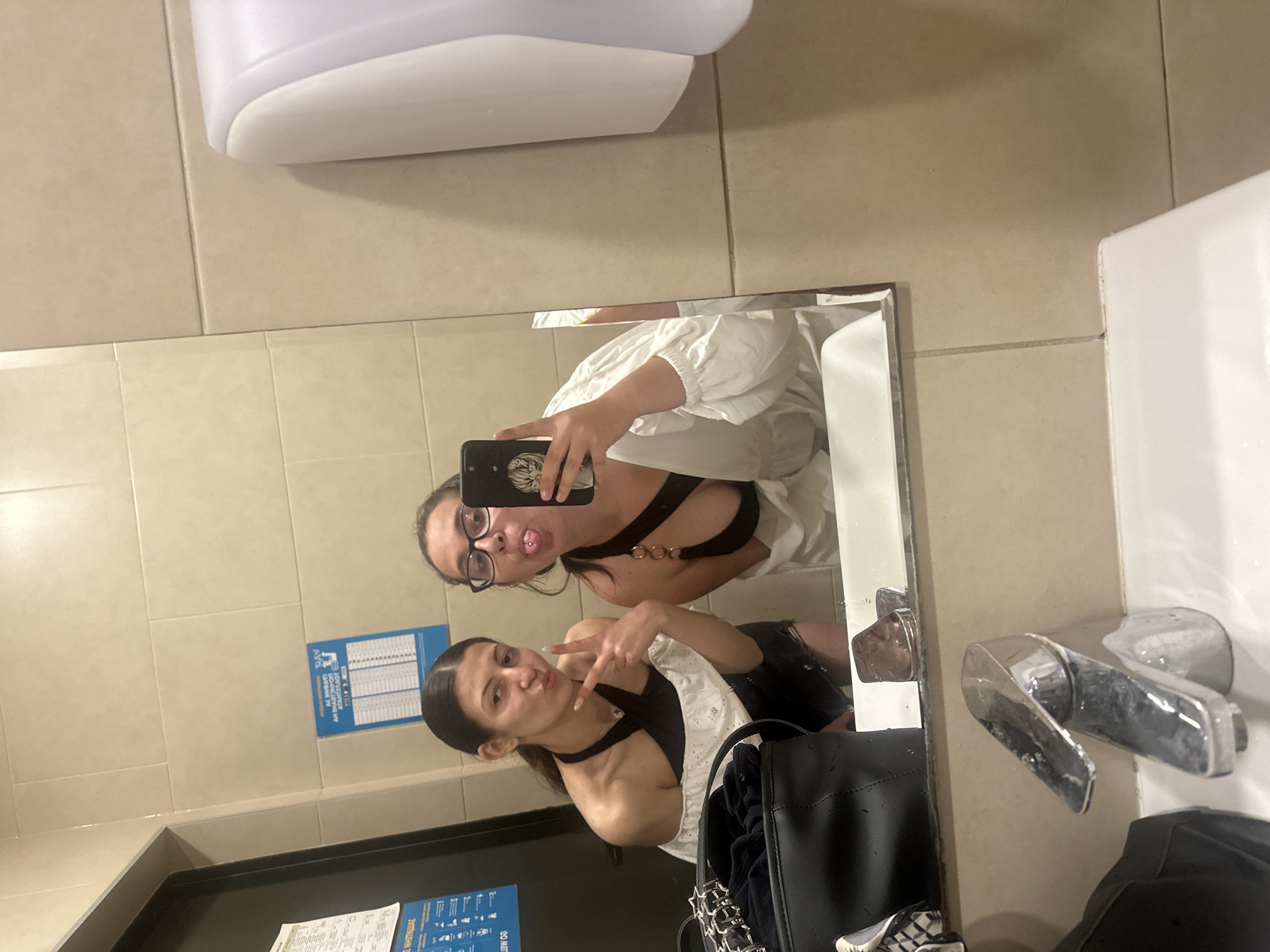 Two women take mirror selfies in Pomorie restroom