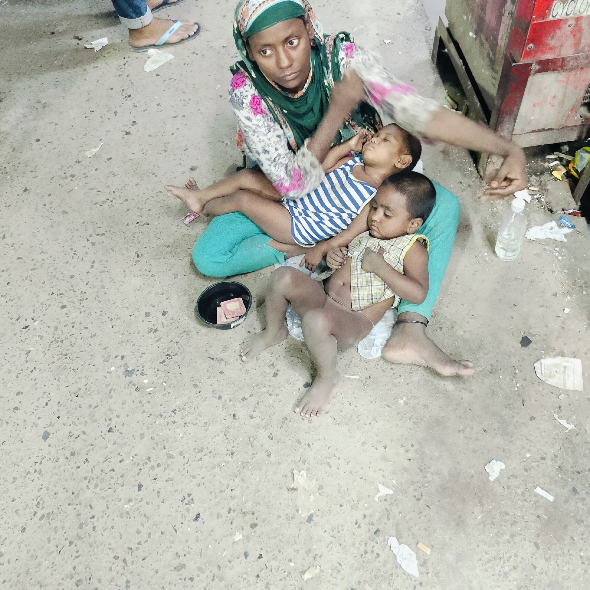 Mother tends children, cat rests on ledge in Dhaka