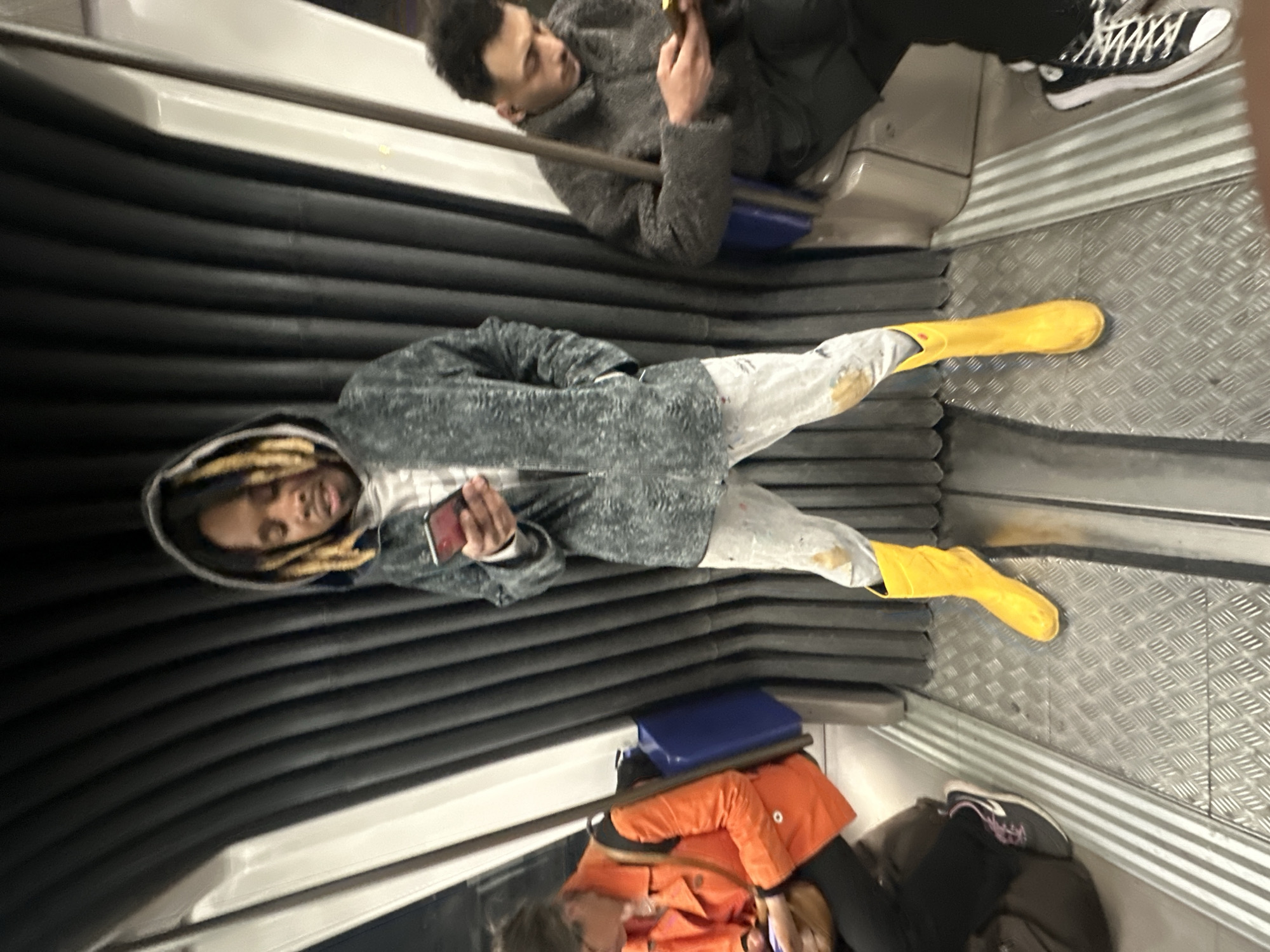 Metro passenger in yellow boots checks phone during evening commute