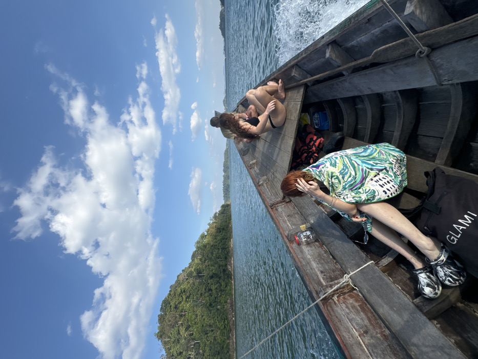 Longtail boat crosses large lake under partly cloudy skies