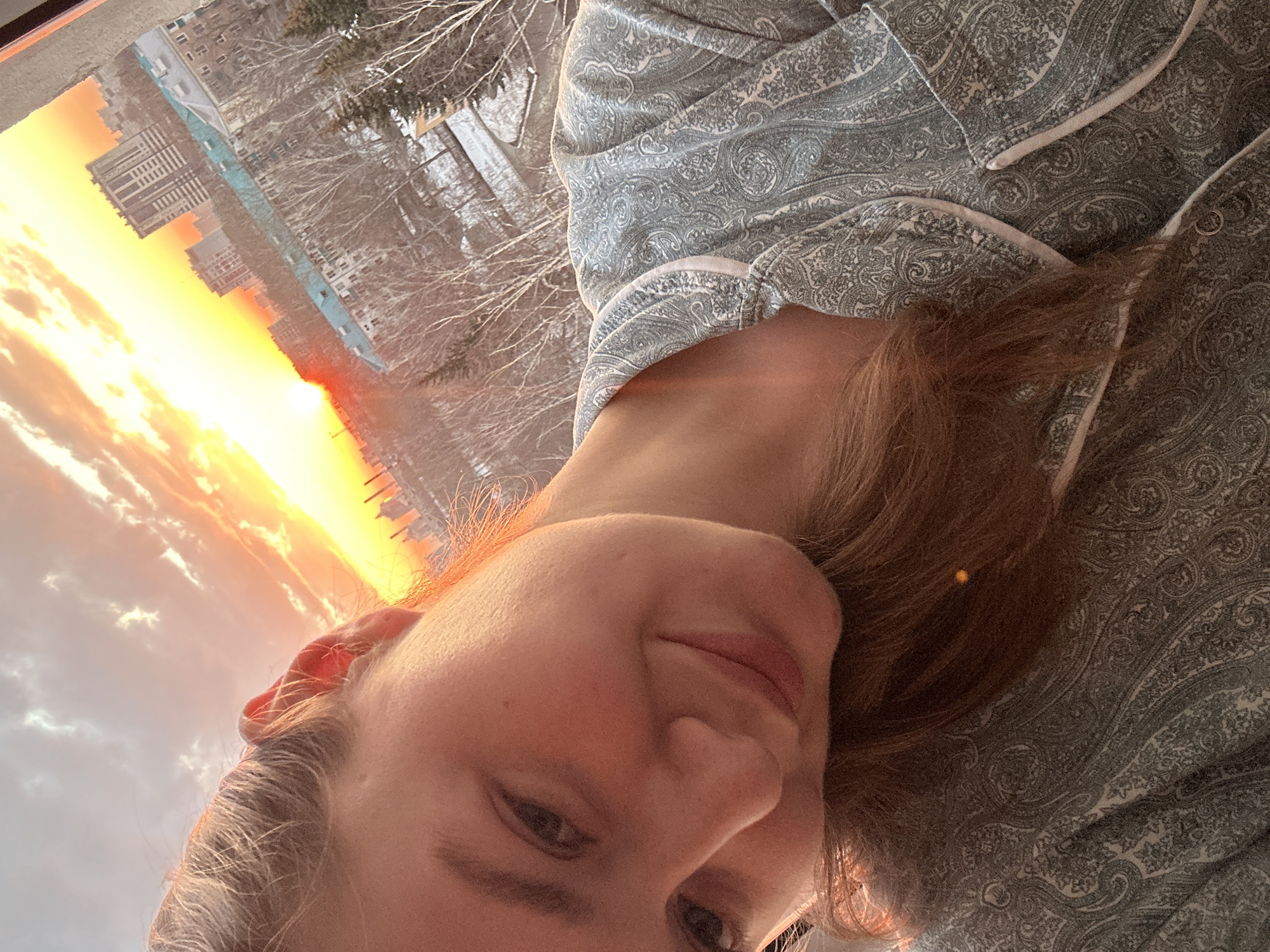 Person takes sunset selfie in pajamas overlooking cityscape