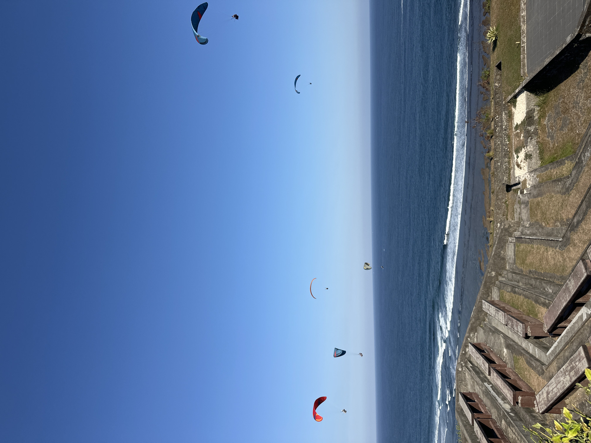 Uluwatu's clifftop amphitheater, cave structure, and paragliders on a clear morning