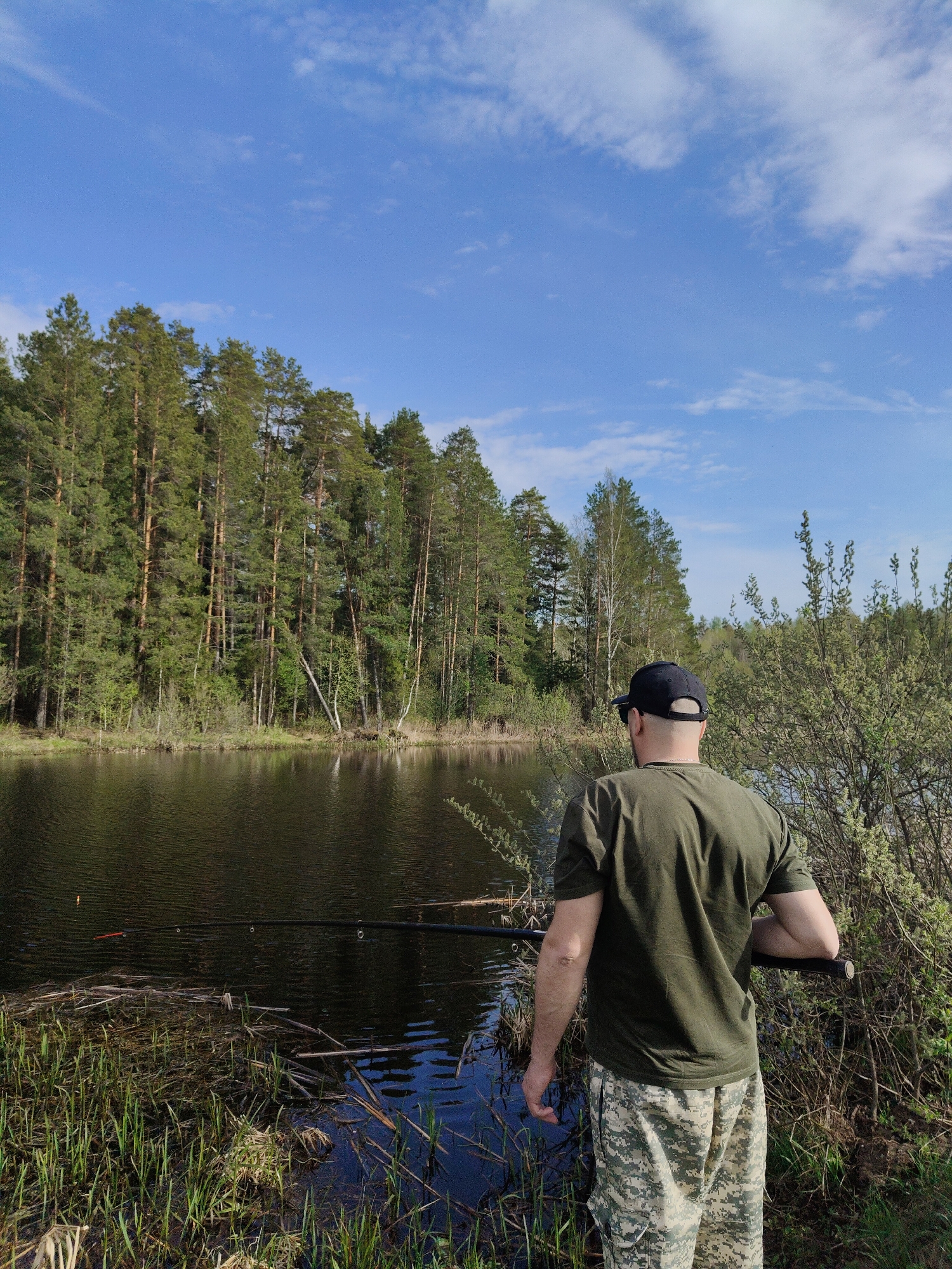 Man fishes near moored barges at lakeside location