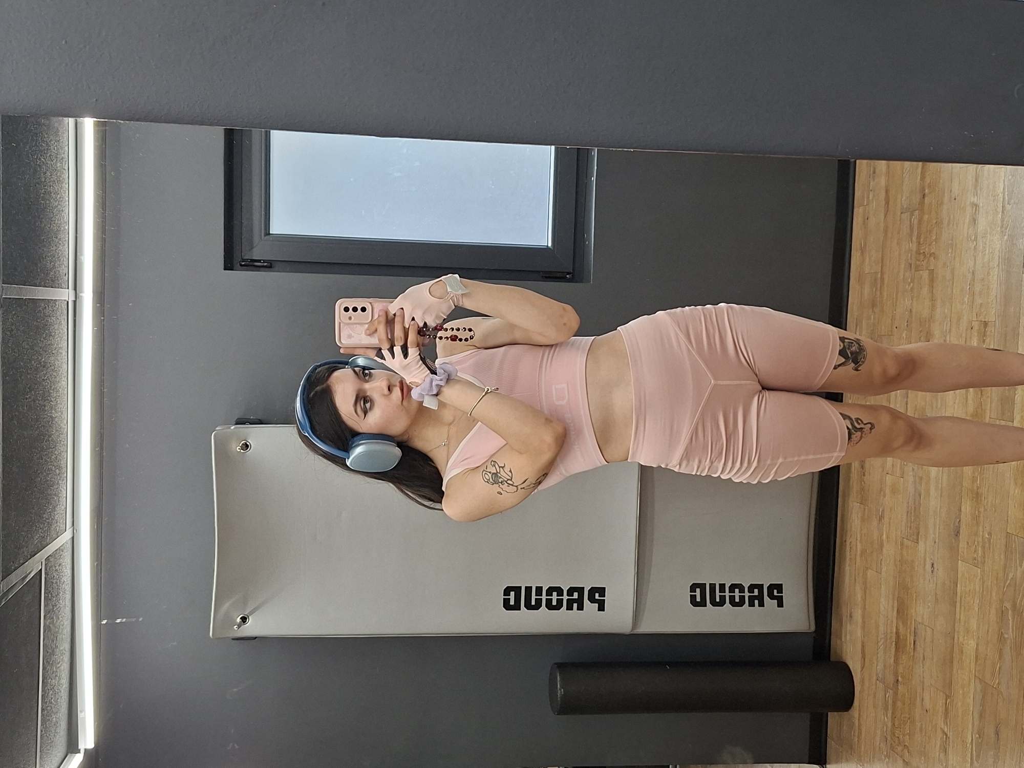 Gym mirror selfie in a pink workout set with blue headphones.