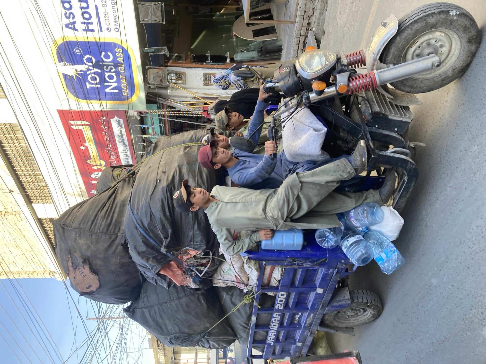 Three men ride overloaded motorcycle with trailer in Quetta