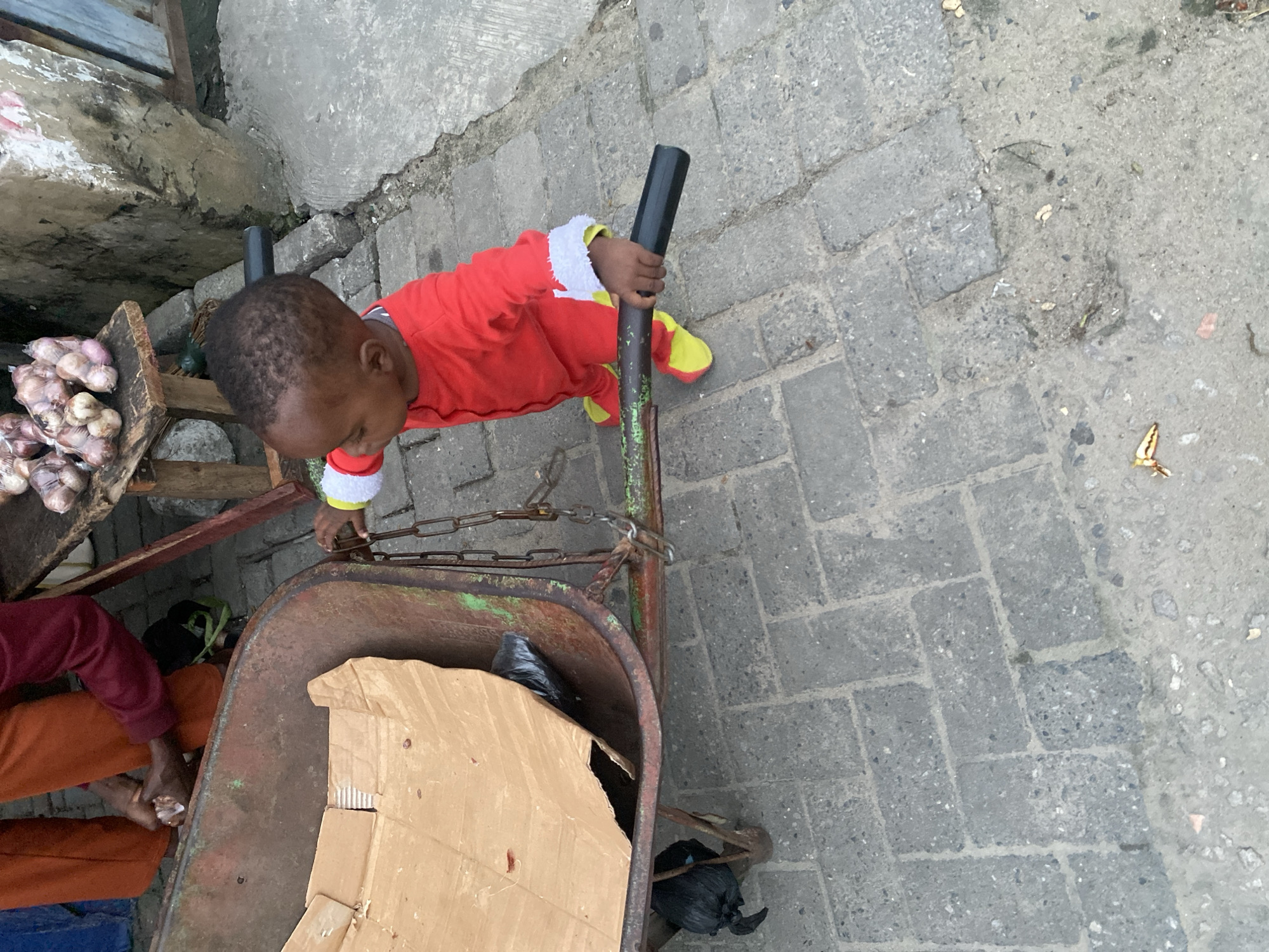 Toddler plays with wheelbarrow near a street food stall