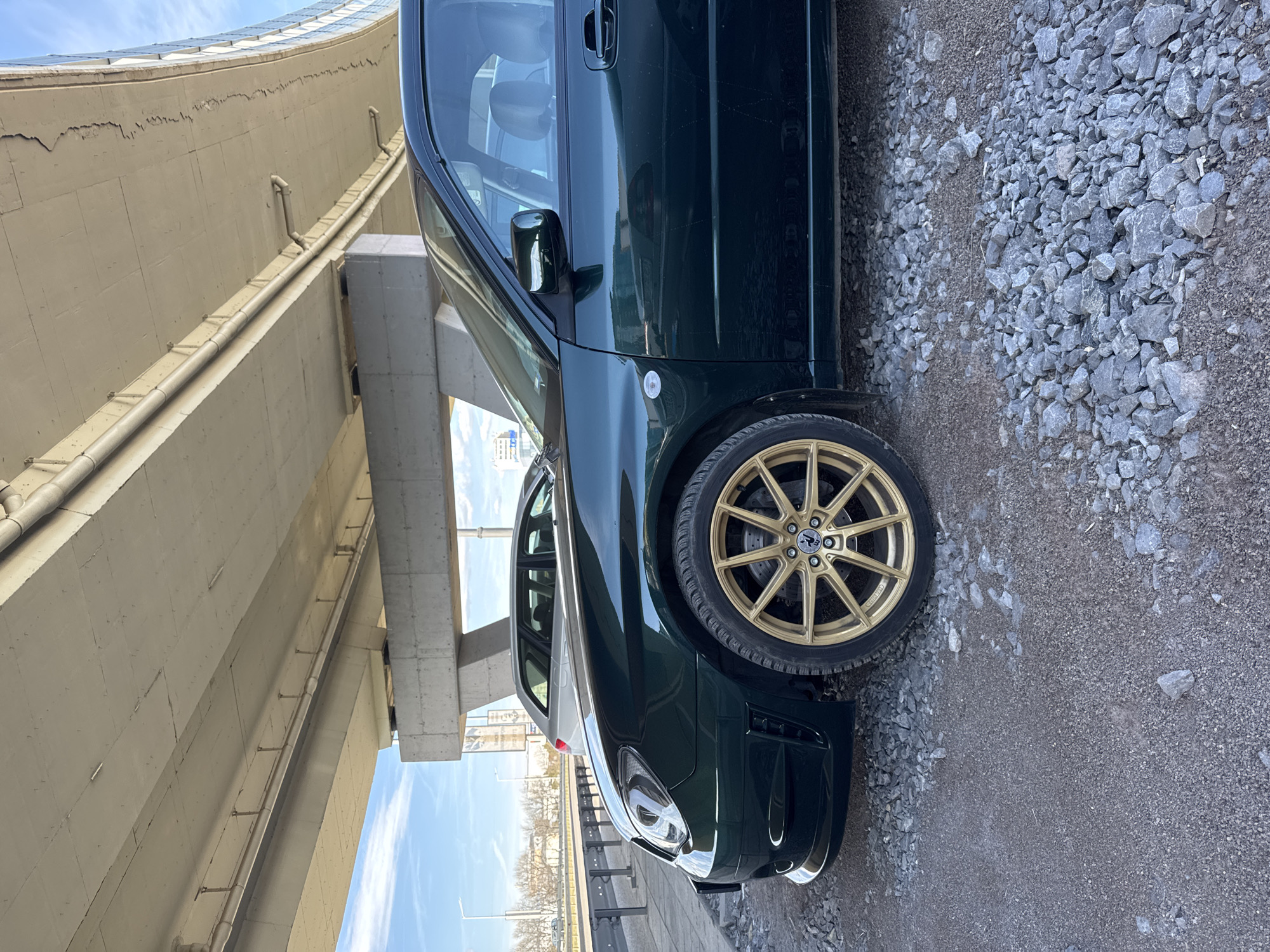 Green car with gold rims parked under Sofia bridge