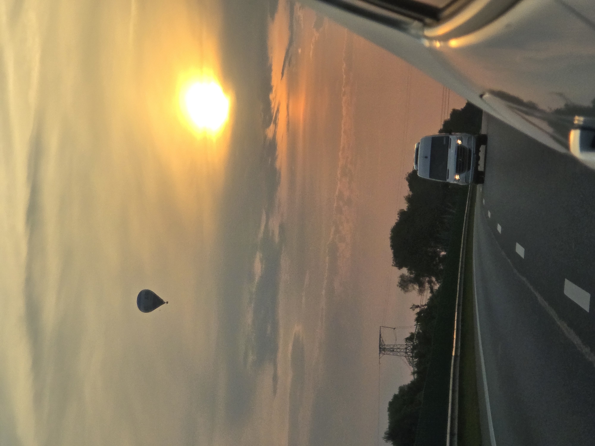 Hot air balloon drifts over a Lithuanian highway at sunset