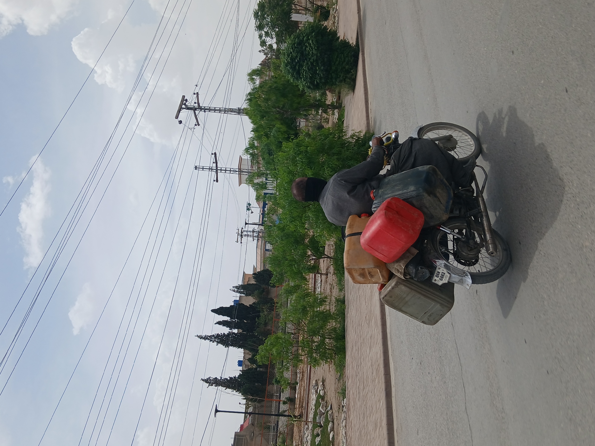 Motorcyclist carries containers on Quetta road beneath power lines