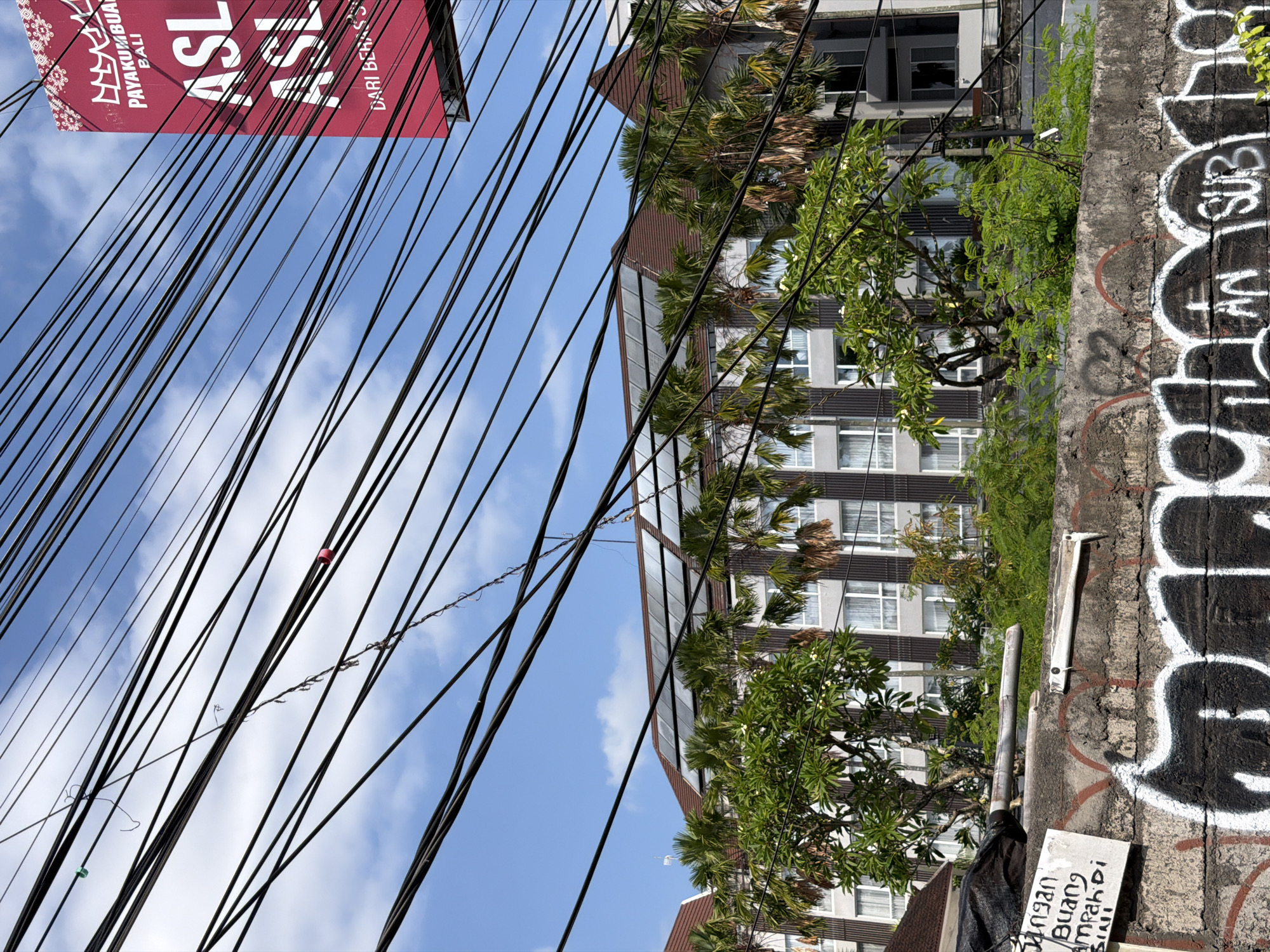 Street-level Kuta: wires, a local carving, and roadside vehicles