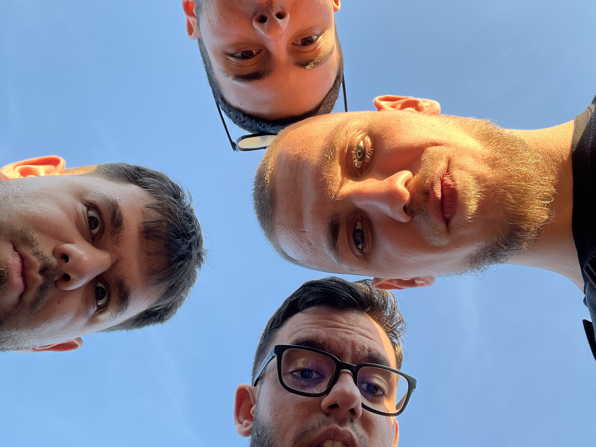 Four men pose in circle formation for upward photo
