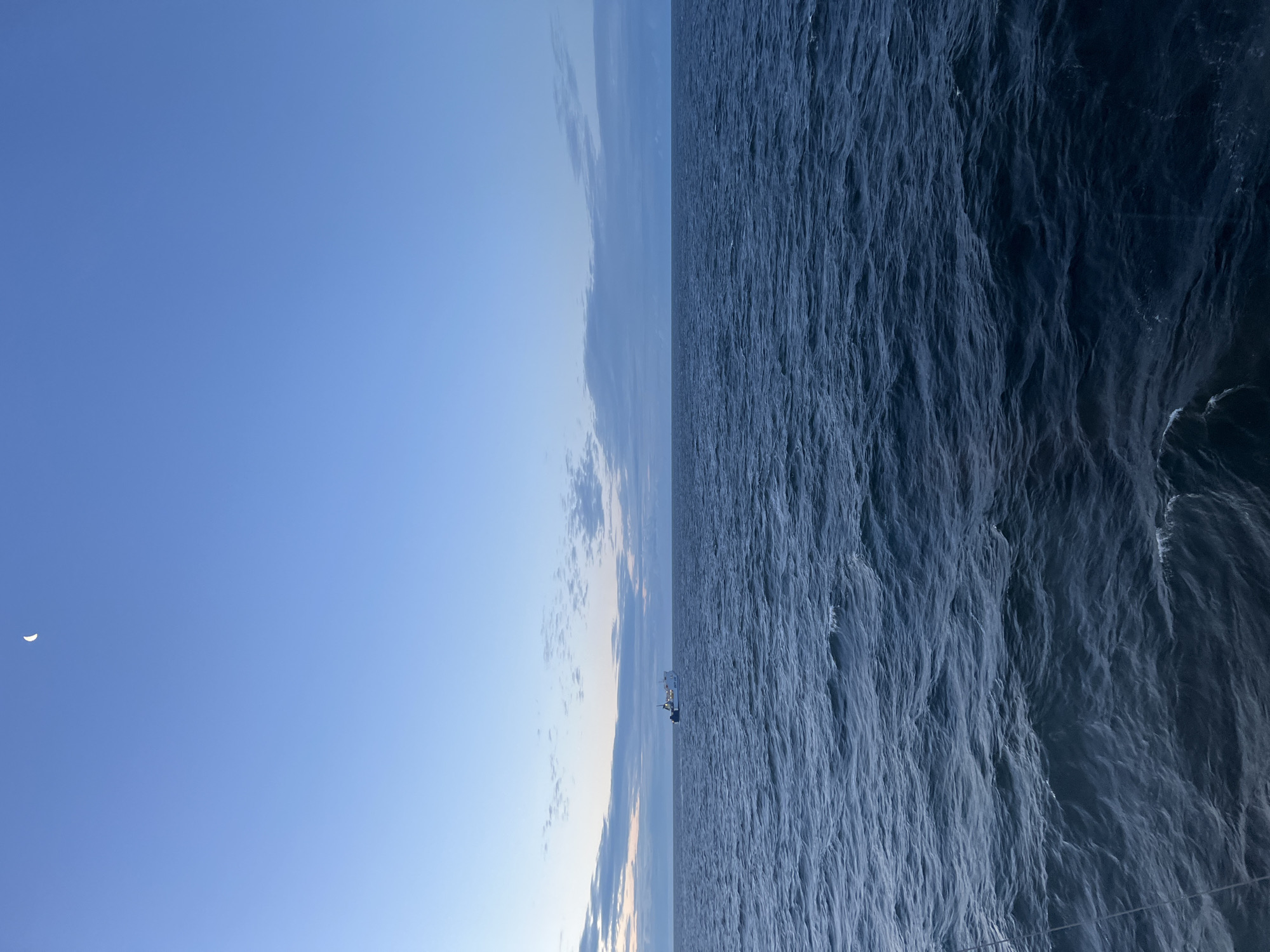Crescent moon rises over a still ocean at dusk