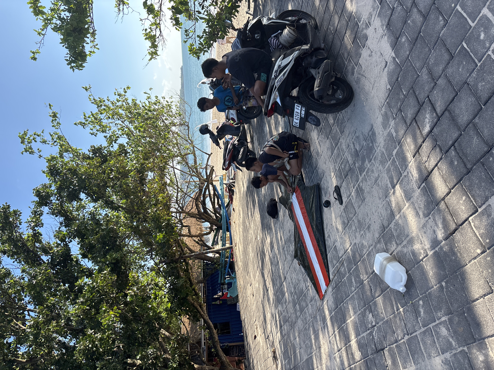 Young men gather on Kuta beach pathway during sunny morning