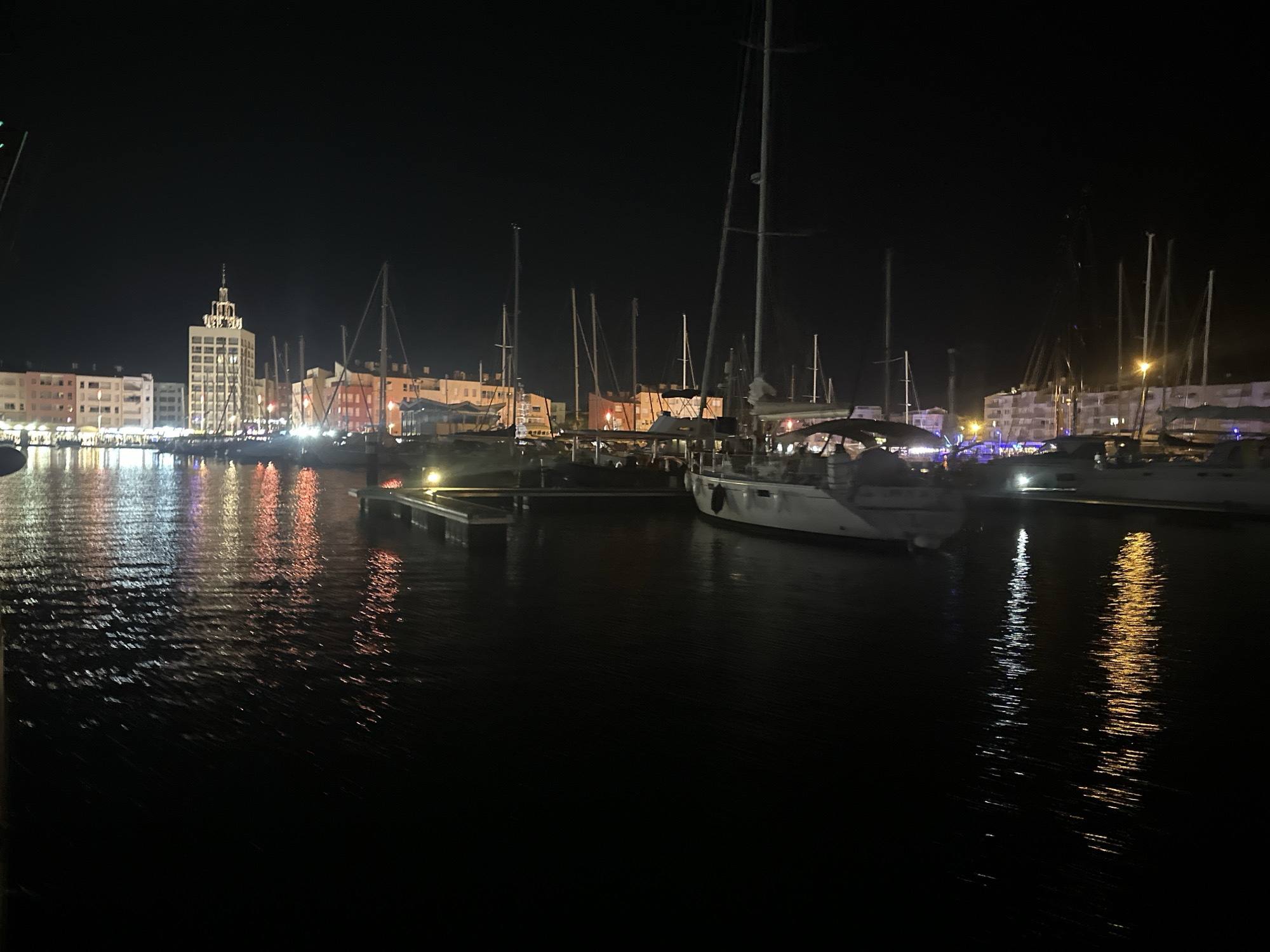 Agde marina at night: Ferris wheel, boats, and a street performer