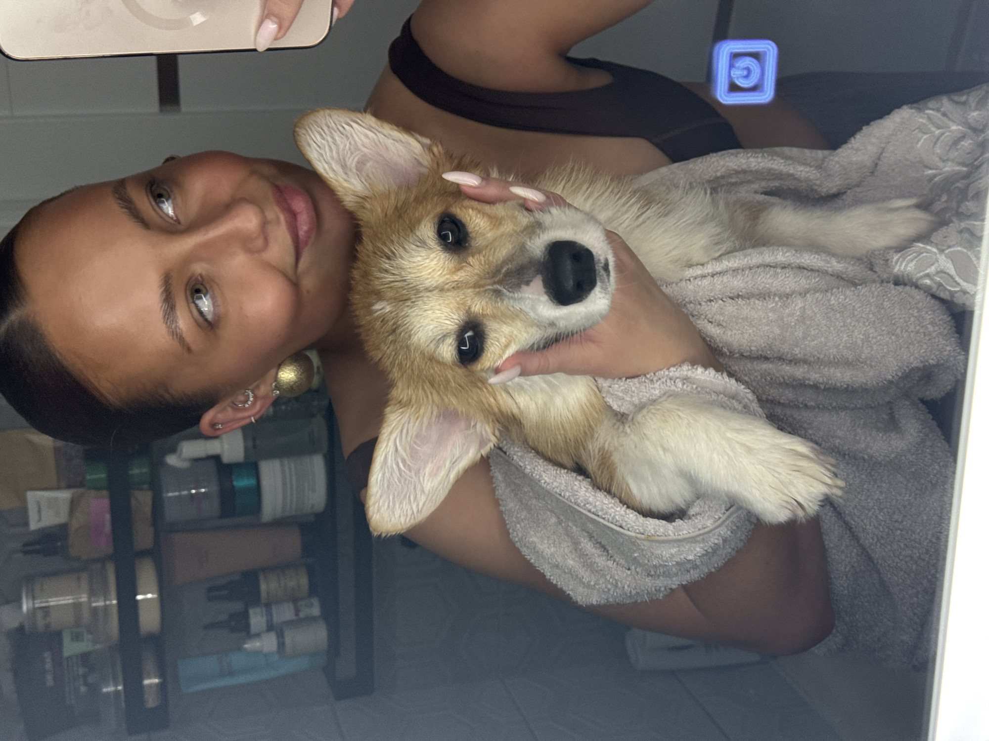 Woman takes bathroom selfie with towel-wrapped corgi puppy