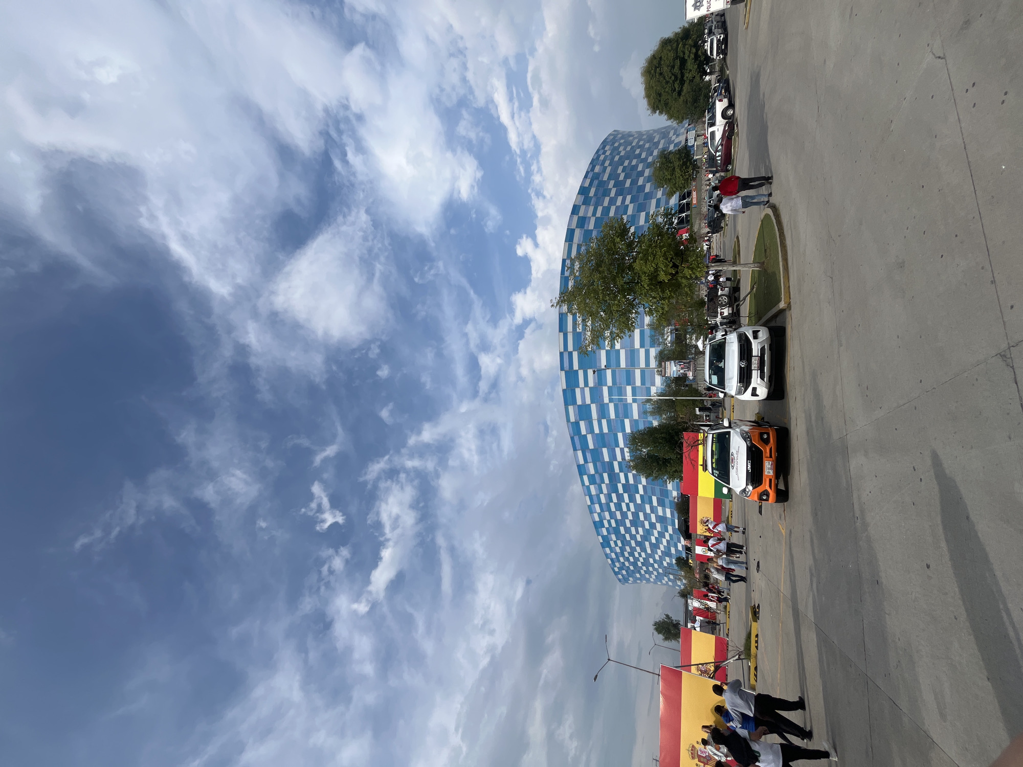 Modern stadium with checkered facade observed with flags, vehicles