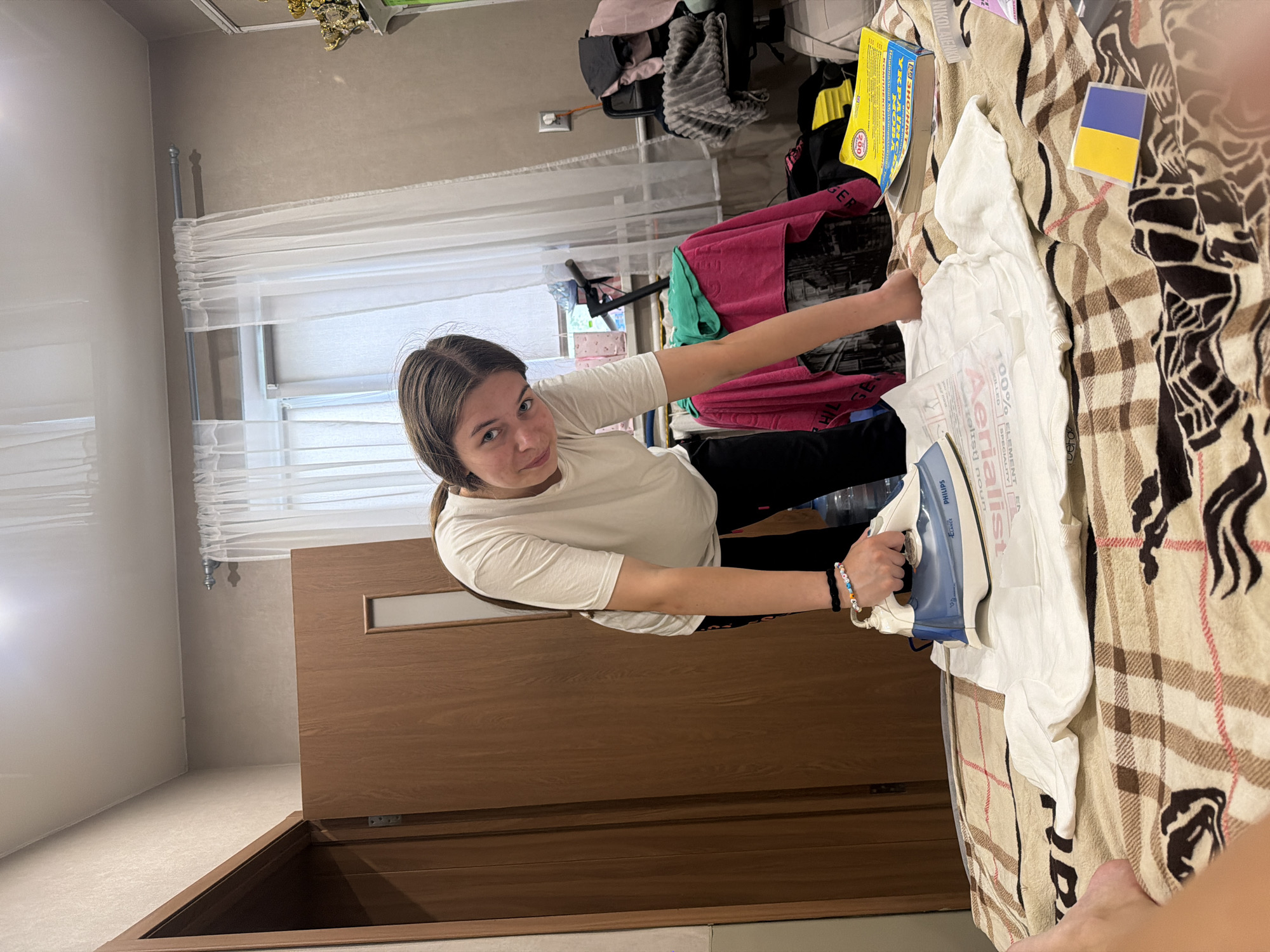 Ironing a t-shirt in a Dnipro bedroom, trophies on the wall