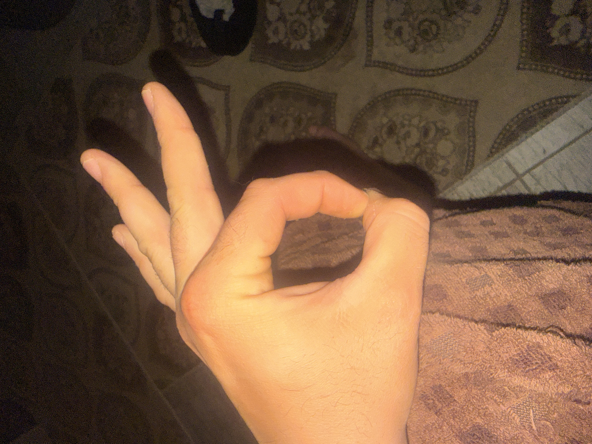 Person Makes OK Hand Gesture Against Patterned Bedding