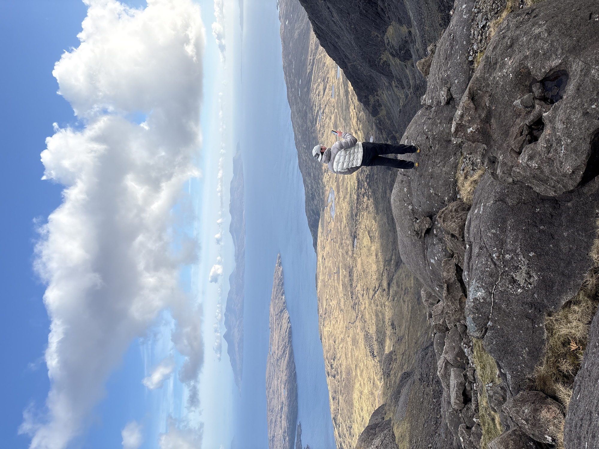 Person stands on rocky outcrop overlooking Scottish coastal landscape