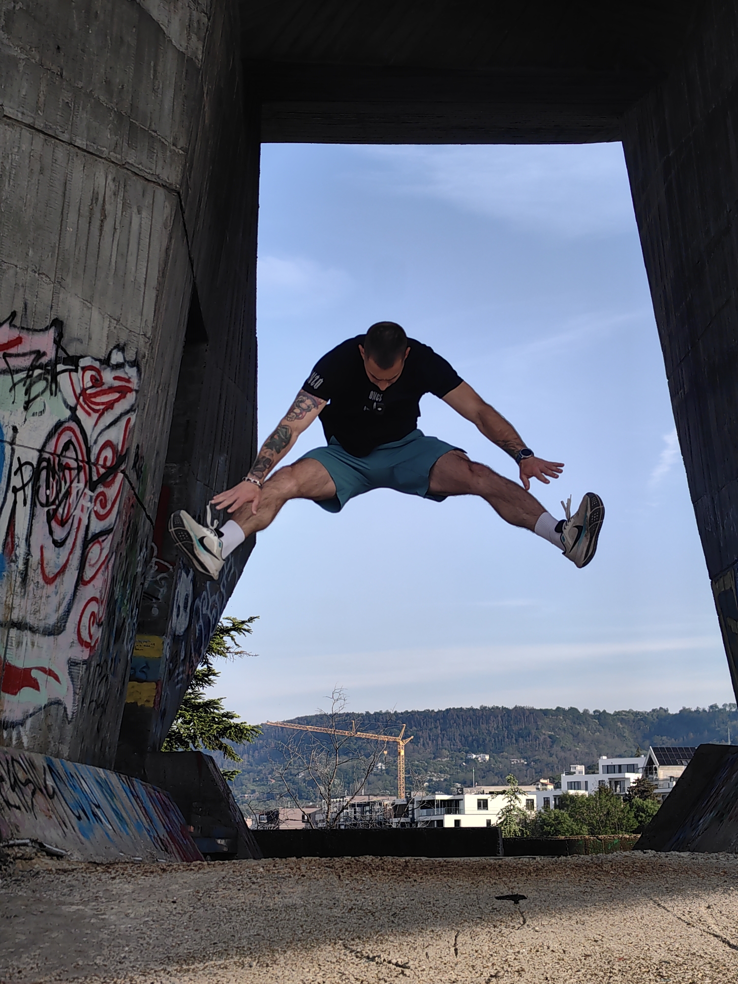 Man performs athletic stunts near graffitied concrete structure early morning