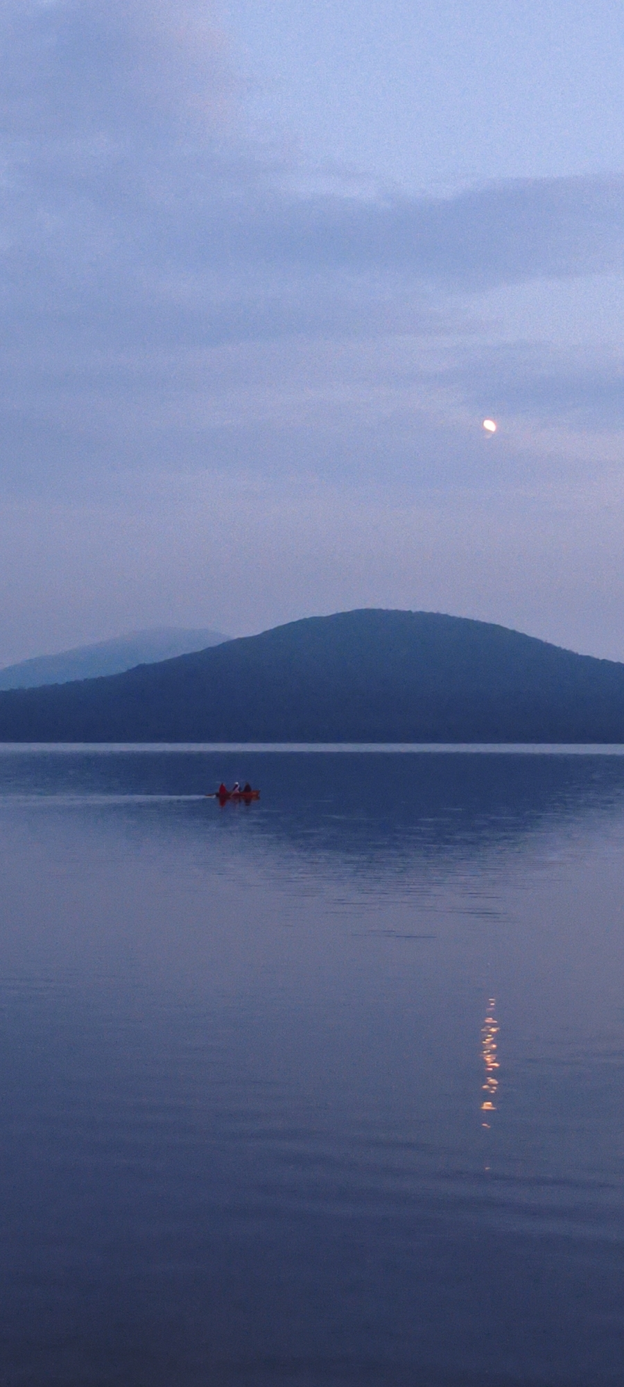 Red canoe crossing calm water at dusk in Zyuratkul'
