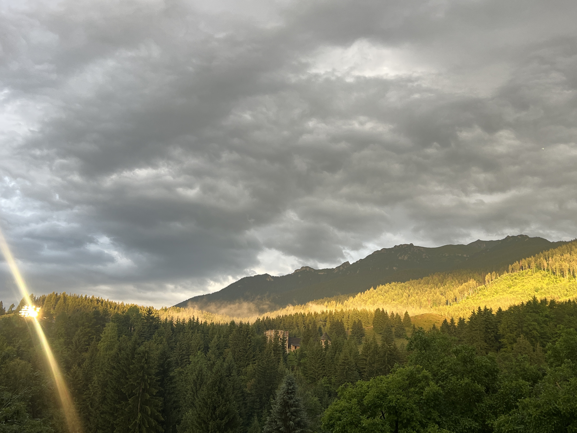Structure fire on forested hillside under dramatic stormy skies