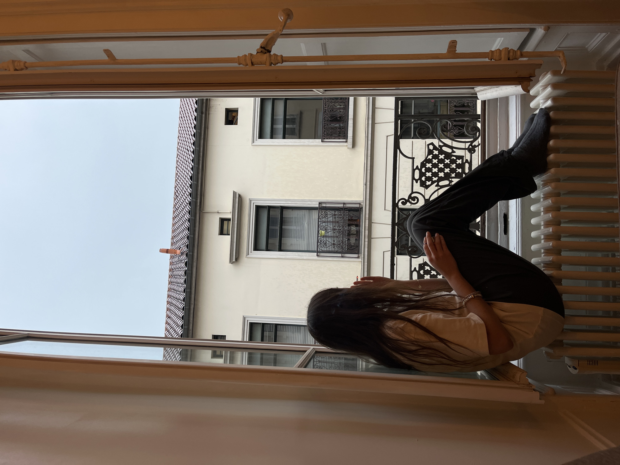Person sits on radiator by open window in Lyon