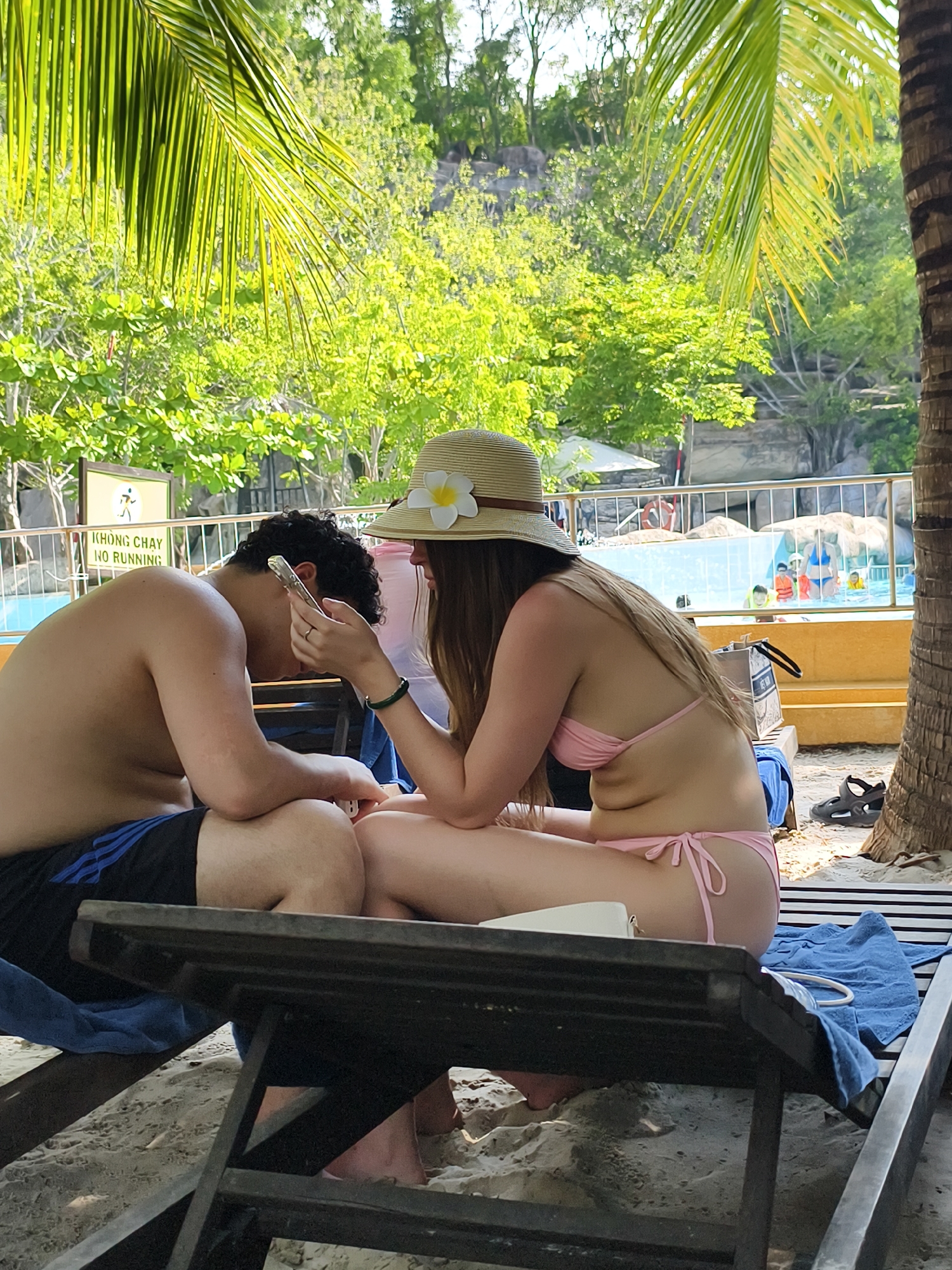Couple enjoys morning beach time, woman grooming while man checks phone