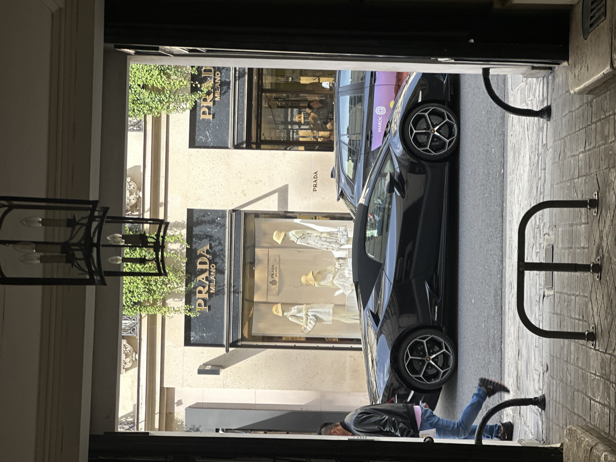 Man lies on Paris street near luxury car, Prada store