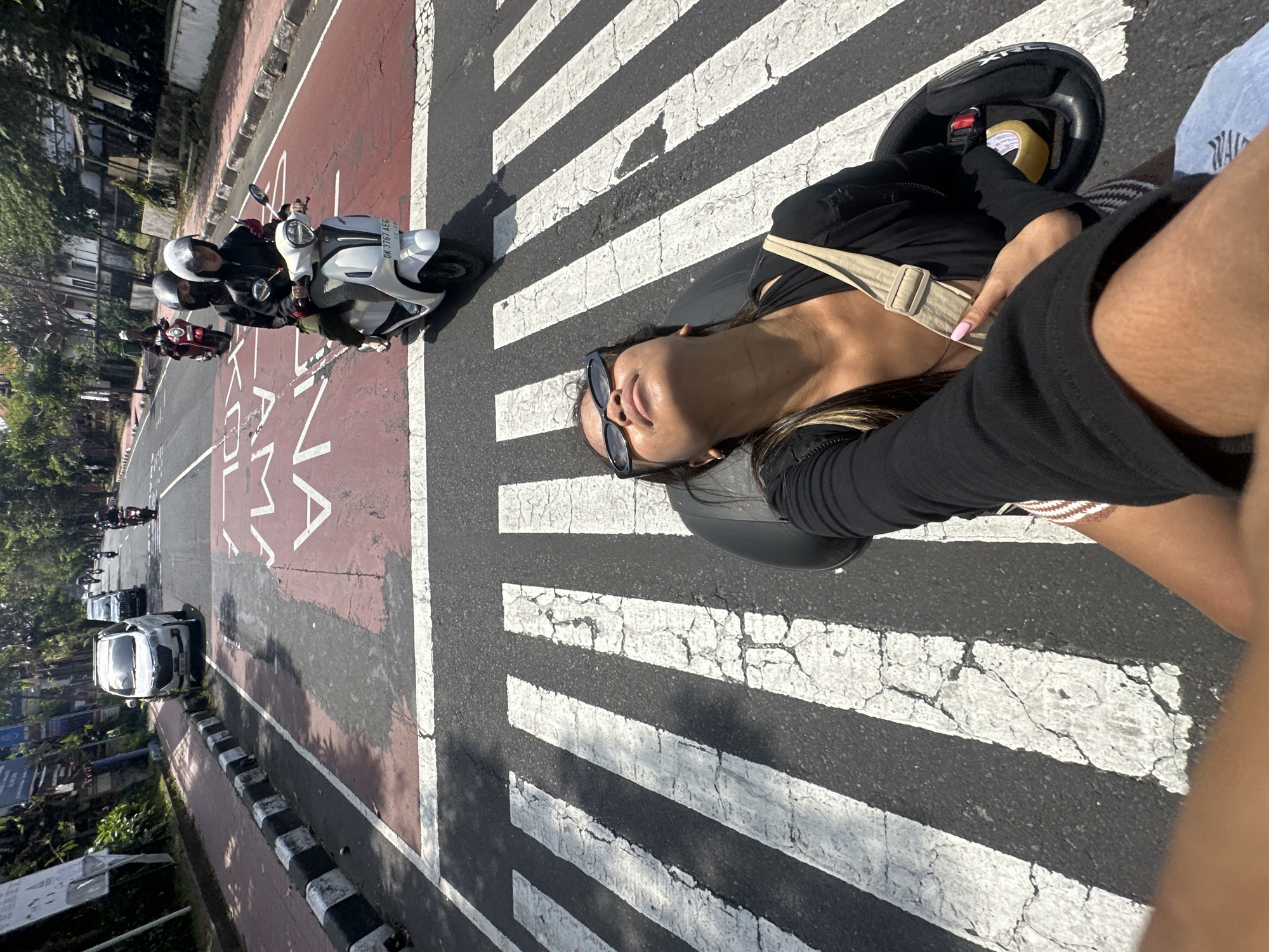 Woman rides motorcycle through Denpasar streets on sunny morning