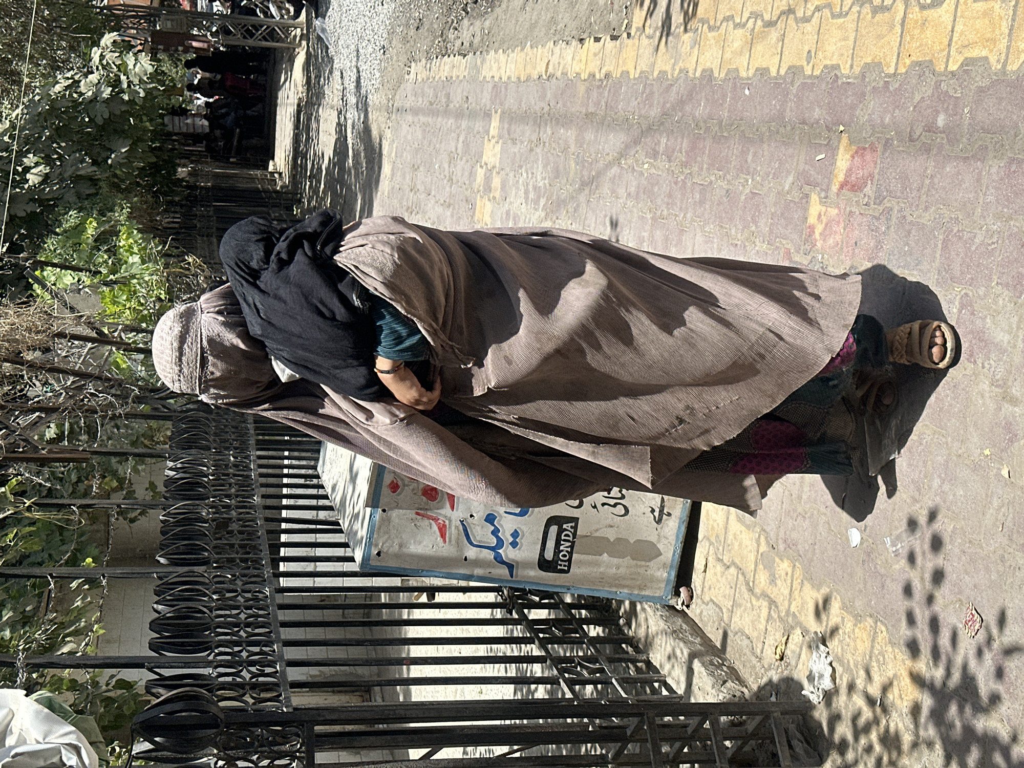 Street scene in Quetta: burqa-clad figure carries child along sidewalk