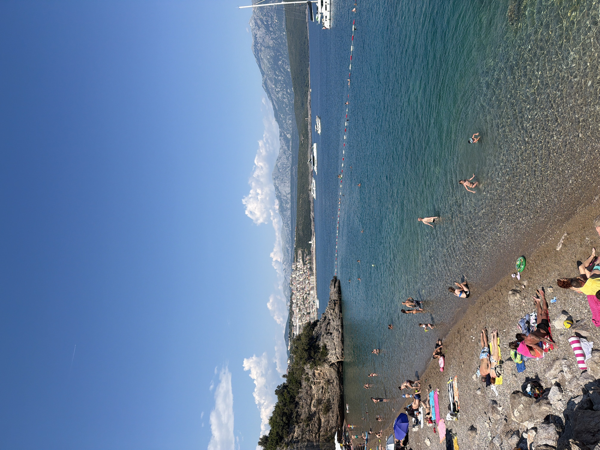 Packed pebble beach and anchored catamarans in Radovići, Montenegro