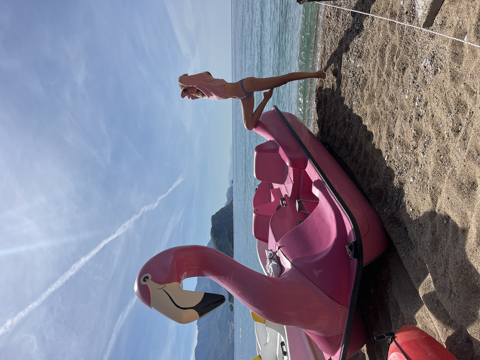 Woman poses with pink flamingo paddle boat on Budva beach