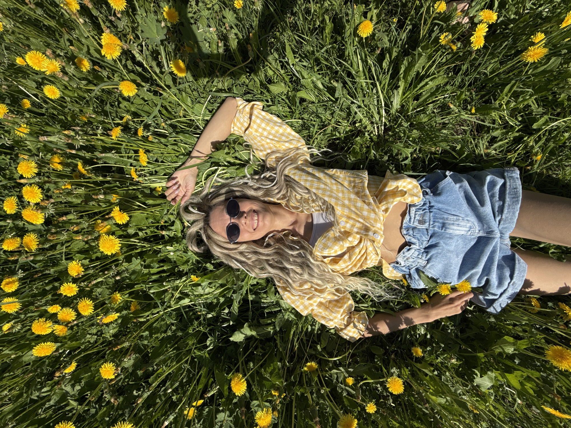 Woman relaxes in dandelion field wearing checkered shirt