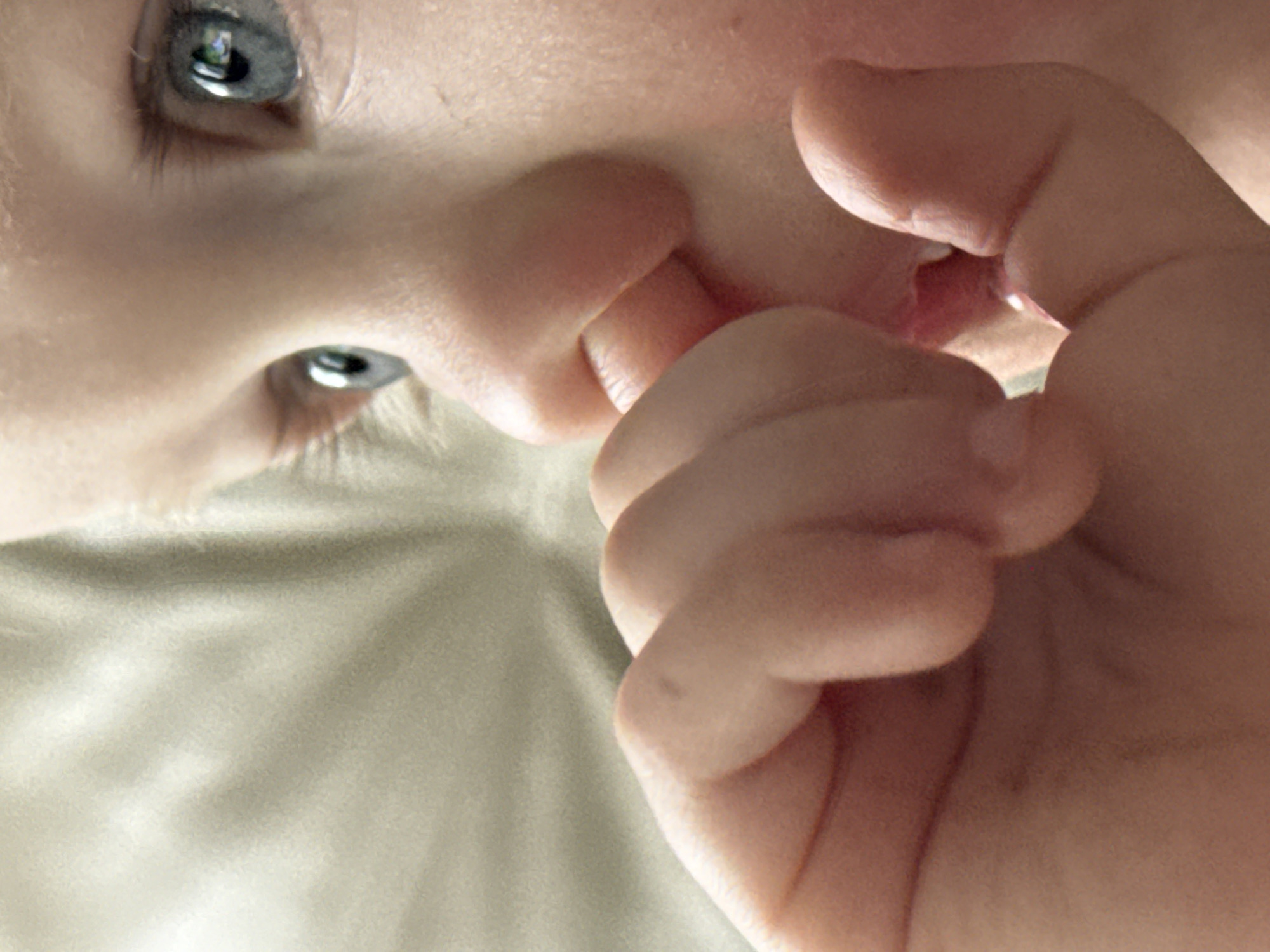 Baby photographed sucking fingers while lying on back
