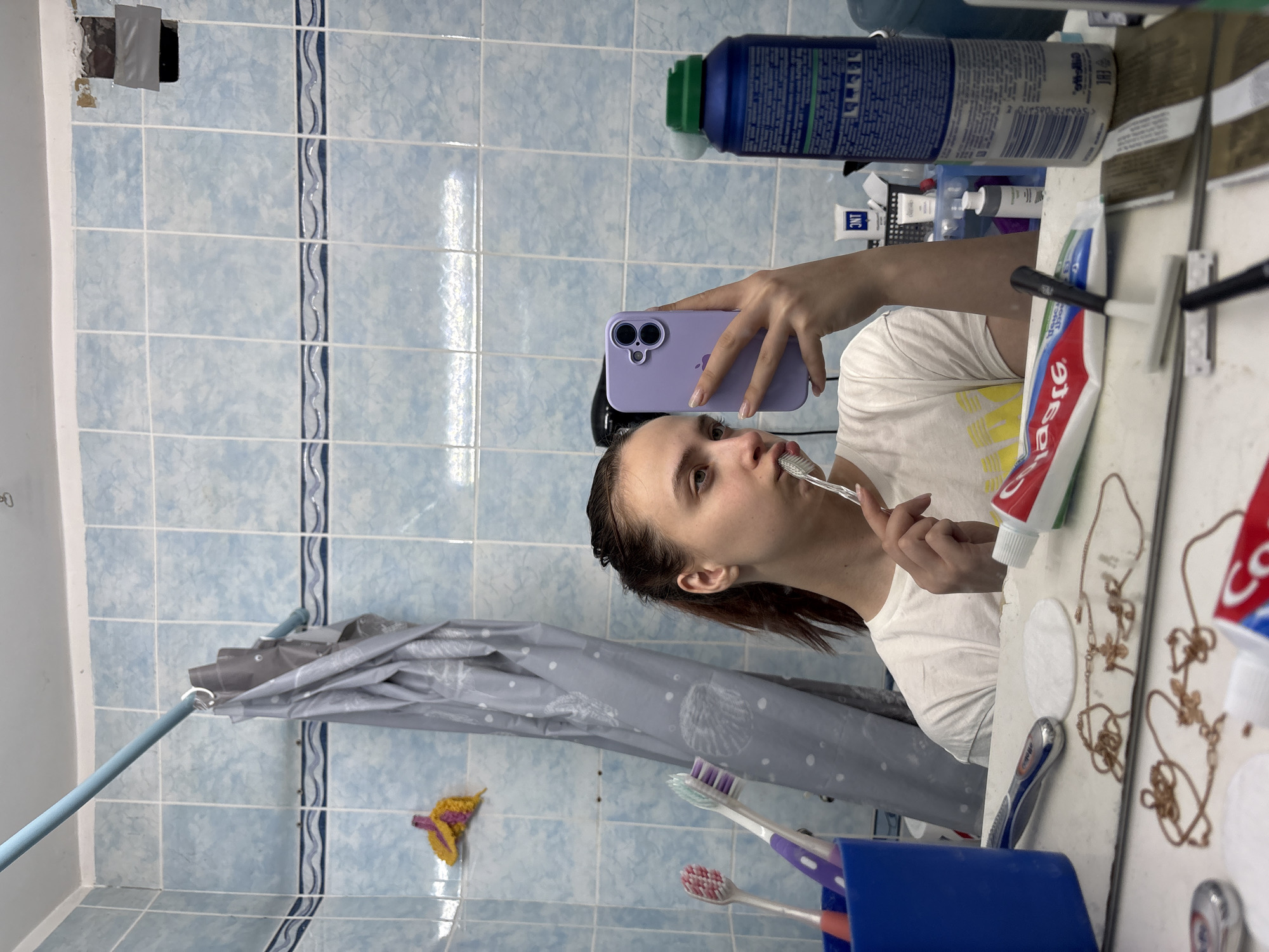 Person takes mirror selfies with purple phone in Russian home