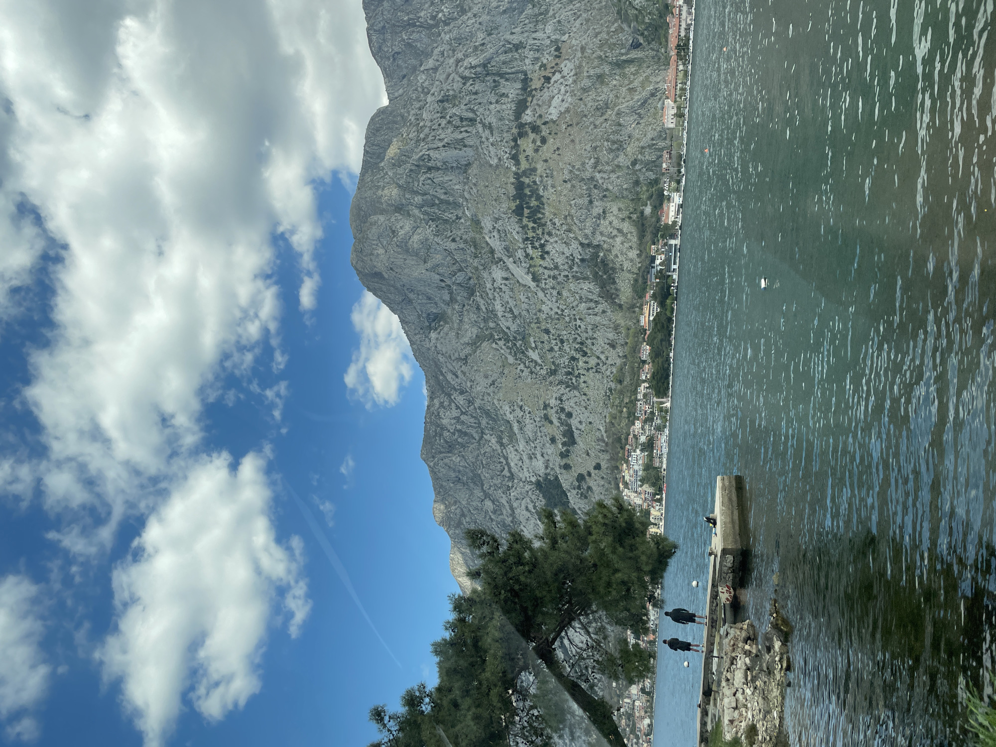 People gather at Škaljari waterfront amid mountain backdrop