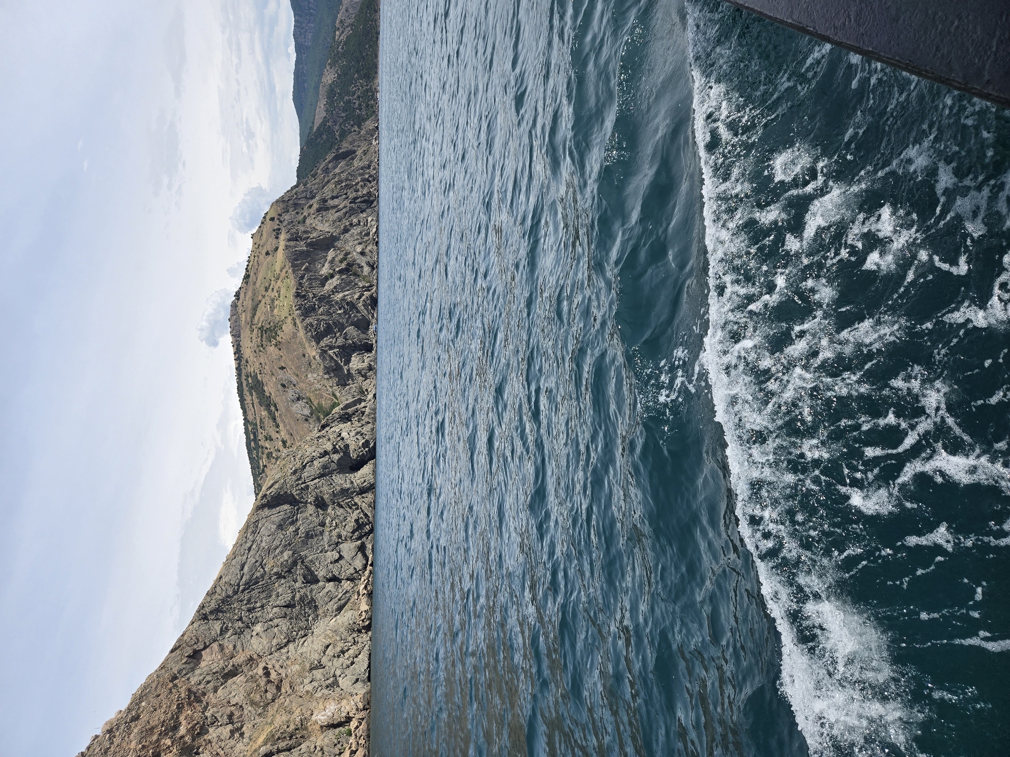 Boat approaches rocky coastline under cloudy skies