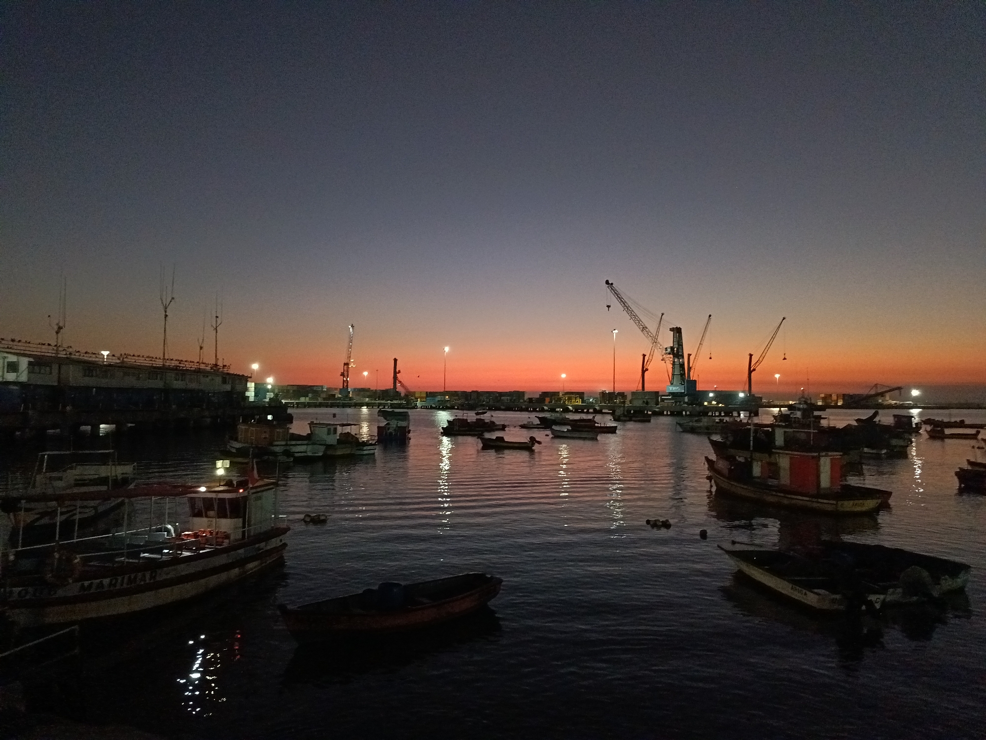 Arica harbor at dusk, boats and cranes under a sunset sky