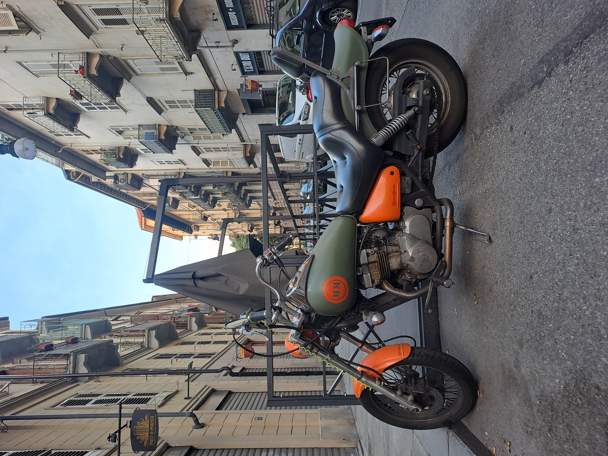 Custom motorcycle and red Vespa parked on a Turin street