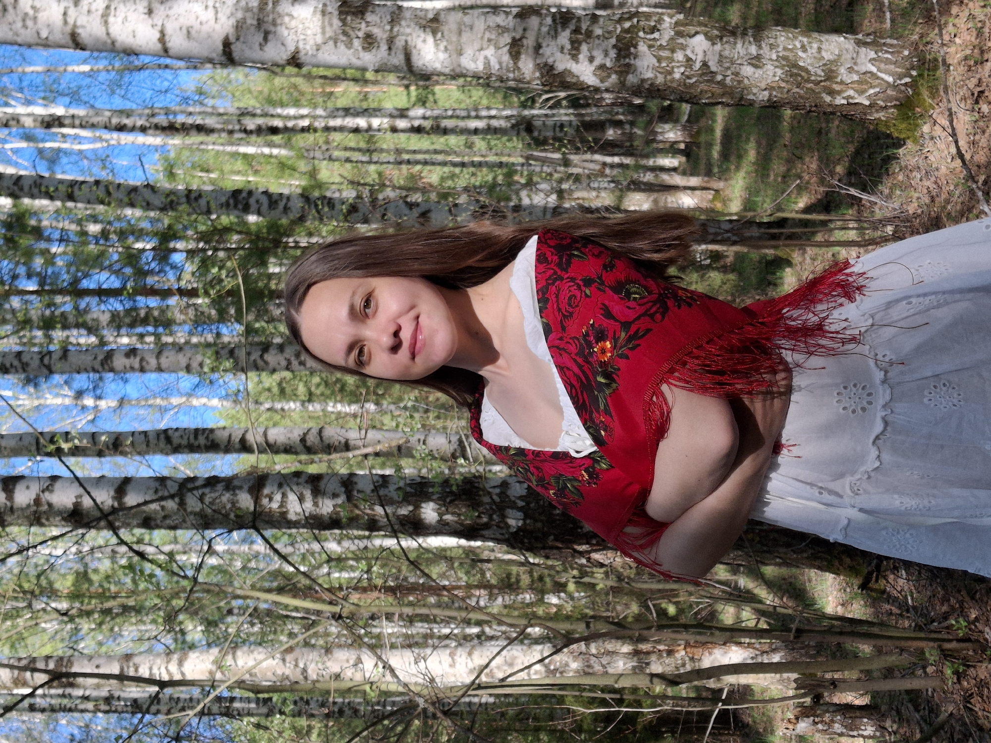 Woman in white dress, red shawl spotted in birch forest