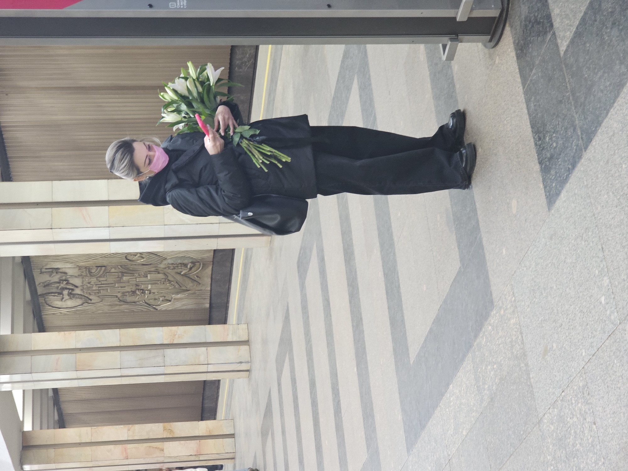 Woman with face mask holds white lily bouquet indoors