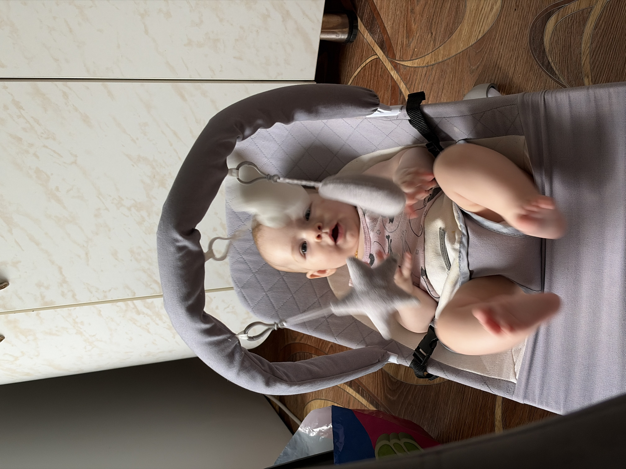 Baby in cat-print onesie relaxes and fusses in grey bouncer