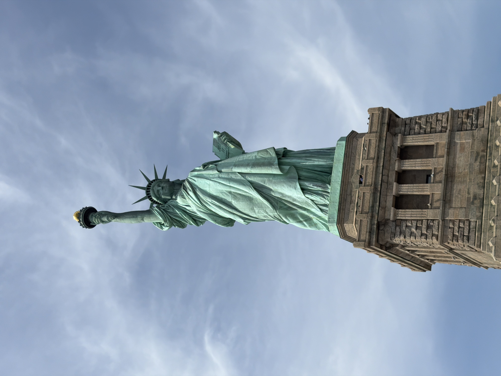 Tourist photographs Statue of Liberty from below against cloudy sky