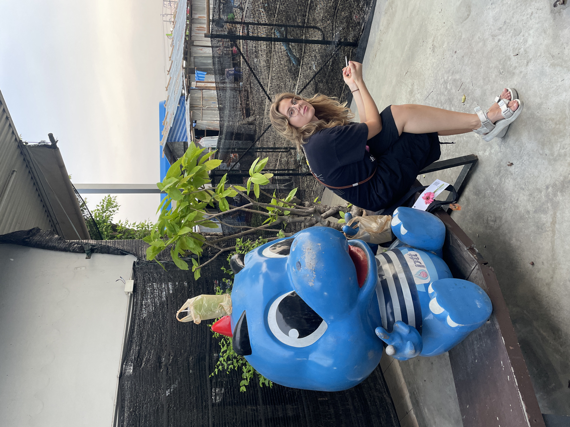 Woman poses with blue cartoon statue in Bangkok street scene