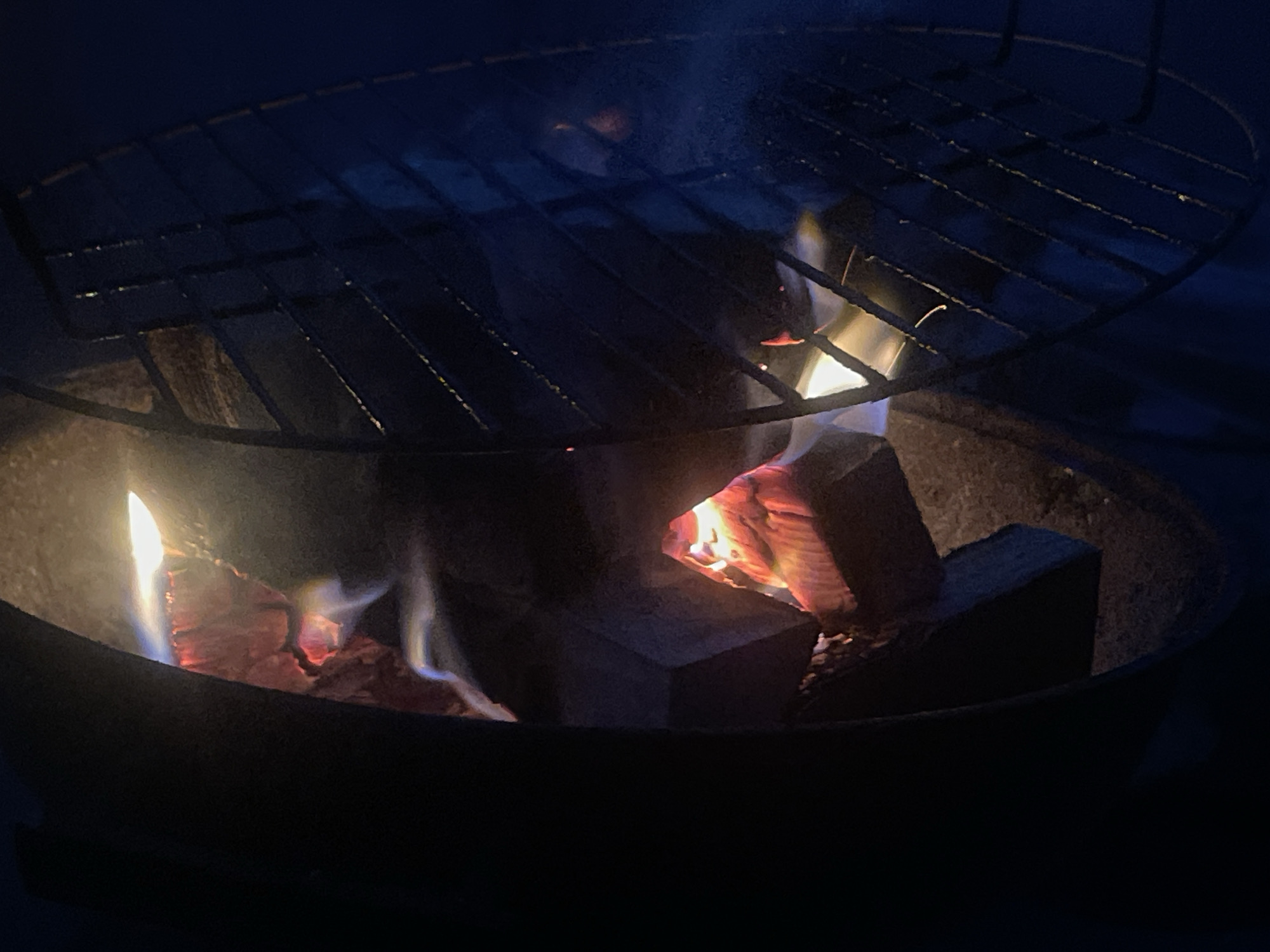 Nighttime fire pit cookout with meat and grill ready to go